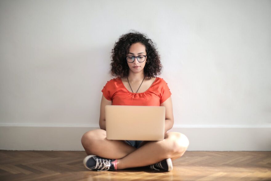 woman in orange crew neck t shirt sitting on brown wooden floor using laptop