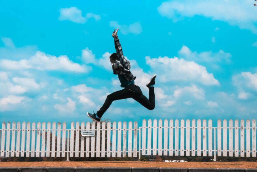 man jumping over white fence