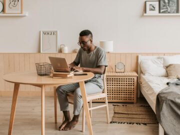 a man in a gray shirt typing on his laptop at home