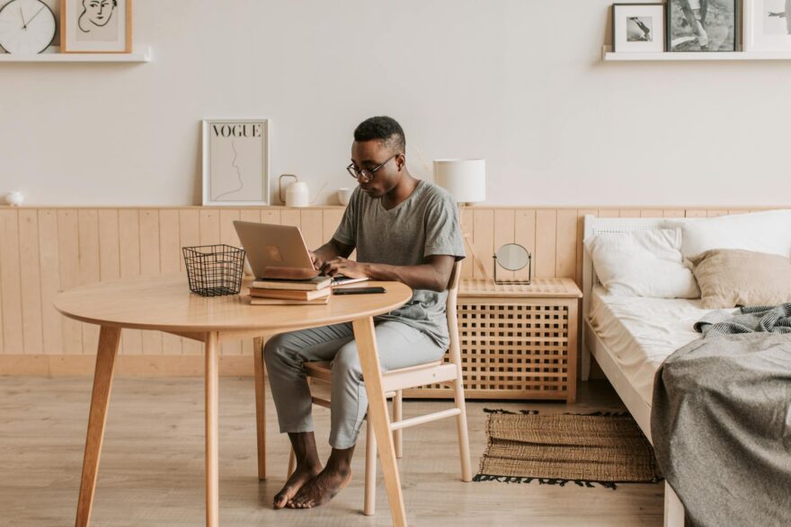 a man in a gray shirt typing on his laptop at home