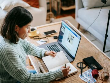 young focused woman writing in planner while using laptop